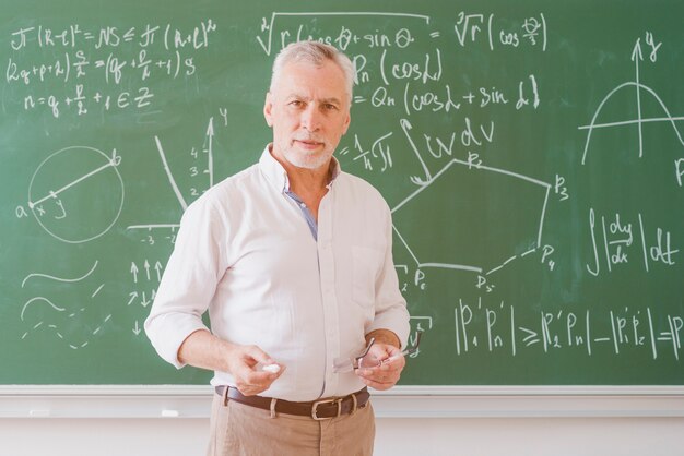 Серьезный учитель-мужчина, стоя на доске с графиком и уравнения и глядя на камеру
