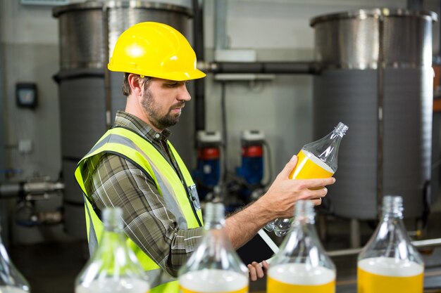 Serious male worker inspecting bottles in juice factory