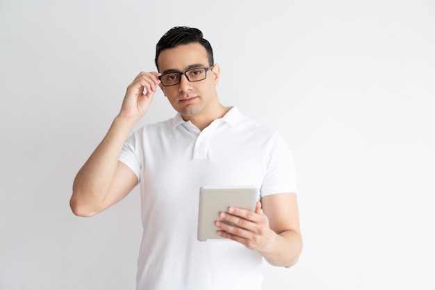 Serious man holding tablet computer and adjusting glasses.