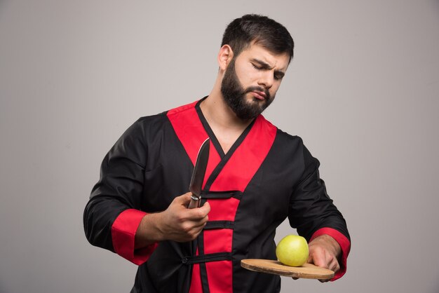 Серьезный человек, держащий деревянную доску с яблоком и ножом.