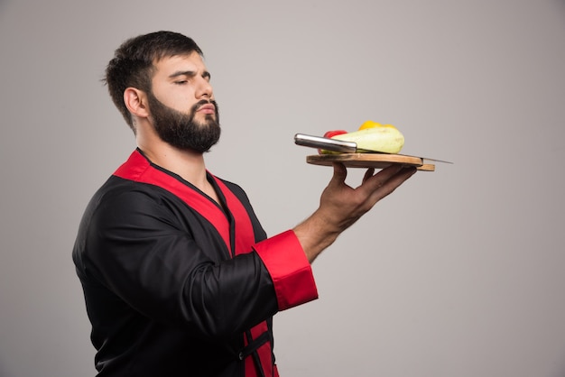 Free photo serious man holding wooden board with yellow pepper, zucchini and knife.