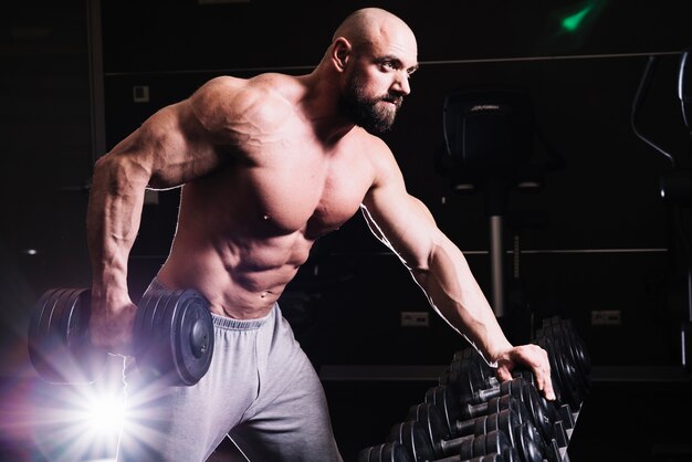 Serious man lifting dumbbell near rack