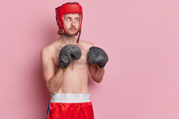 Free photo serious man poses in boxing gloves ready to punch prepares for competition in gym