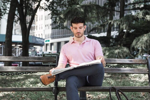 Serious man reading newspaper on park bench