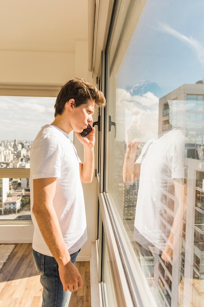 Serious man standing in front of glass window while talking on mobile phone