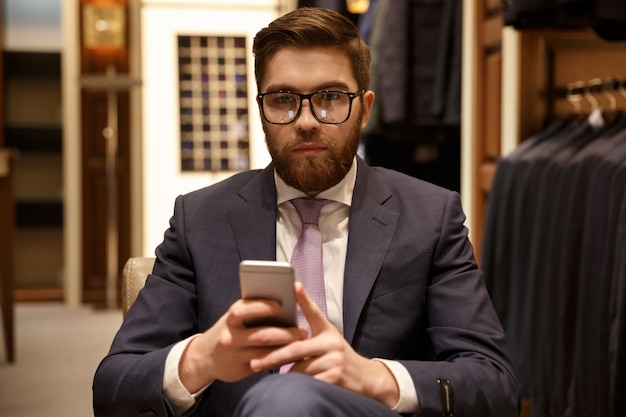 Серьезный человек в костюме и очках держит мобильный телефон