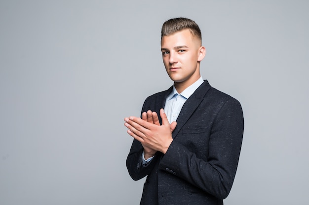 Serious man in suite clap his hands in front of light wall