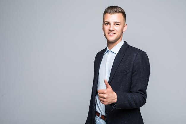 Serious man in suite posing with thumbs up sign in front of light wall