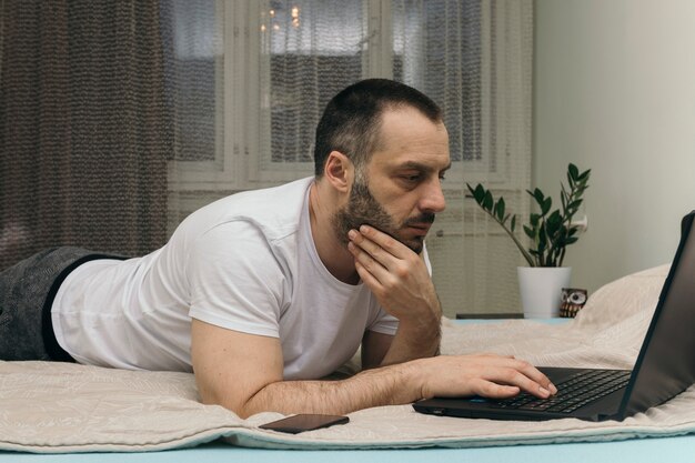 Serious man using laptop on bed