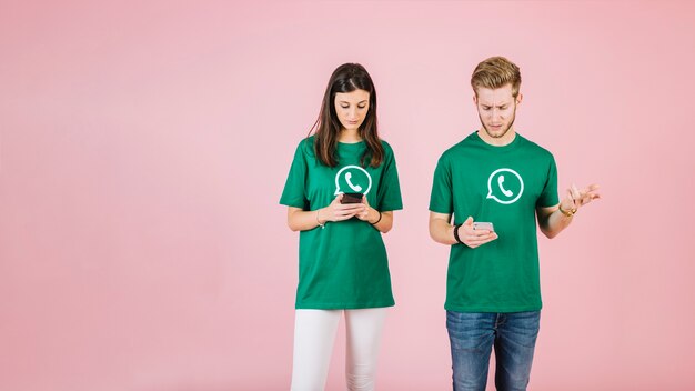 Serious man and woman using mobile phone on pink backdrop