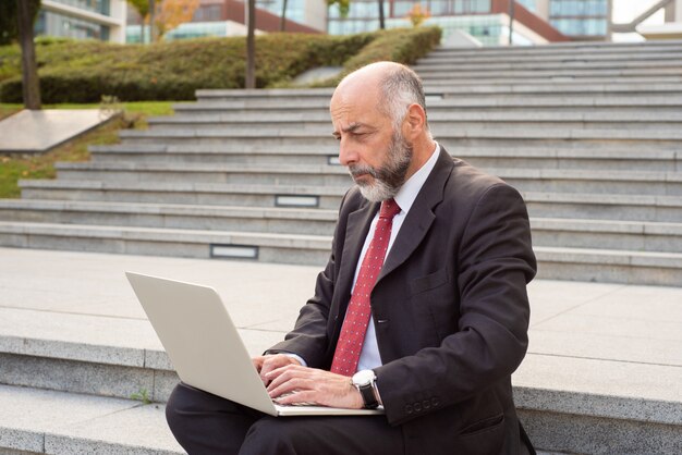 Serious mature businessman using laptop in street