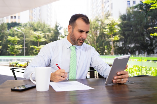 Serious mature freelancer working with digital tablet at cafe