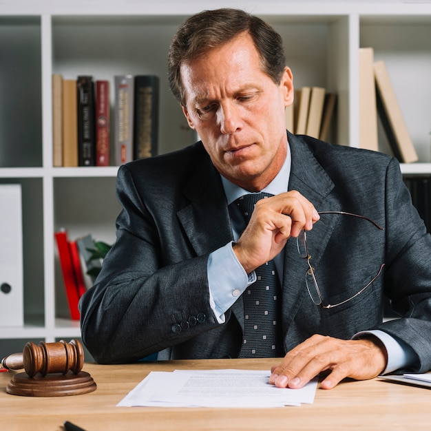 Free photo serious mature lawyer reading document on desk in the courtroom