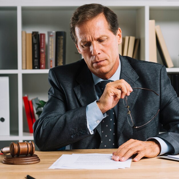 Serious mature lawyer reading document on desk in the courtroom
