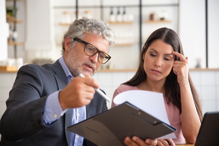 Serious mature legal advisor reading, analyzing and explaining document to female customer