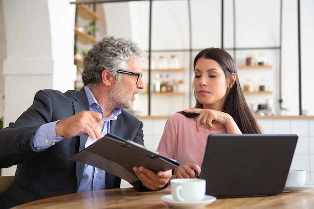 Serious mature legal expert reading, analyzing and explaining document to female customer