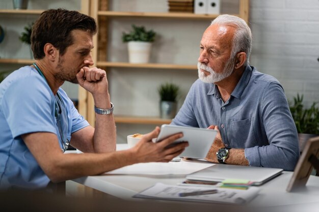 Serious mature man having consultations with his doctor who is showing him medical test analysis on digital tablet