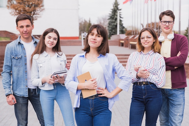 Серьезные мужчины и женщины, стоя с книгами, глядя на камеру