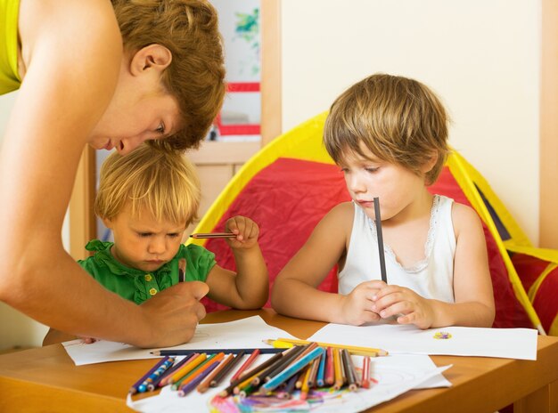 Serious mother and children drawing with pencils