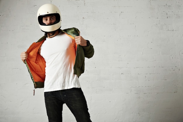 Серьезный мотоциклист показывает оранжевую подкладку своей куртки цвета хаки в старинном шлеме, изолированном на белом