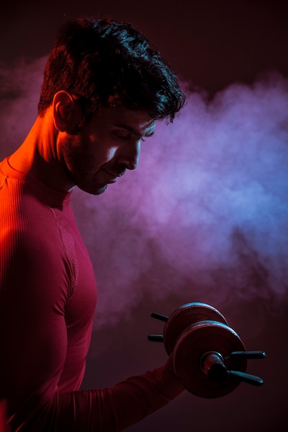 Free photo serious muscular man with dumbbell in dark