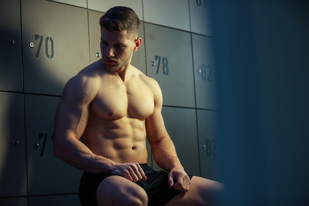 Бесплатное фото Серьезный мускулистый спортсмен отдыхает в раздевалке спортзала перед спортивной тренировкой и думает о чем-то