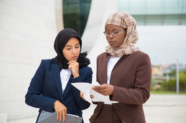 Free photo serious muslim business colleagues reviewing documents outside