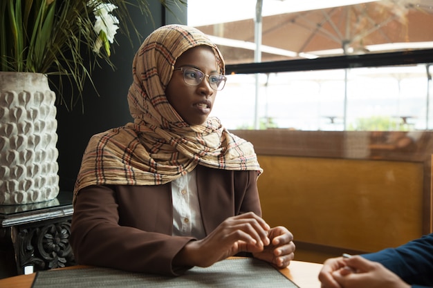 Serious Muslim female employee talking to coworker