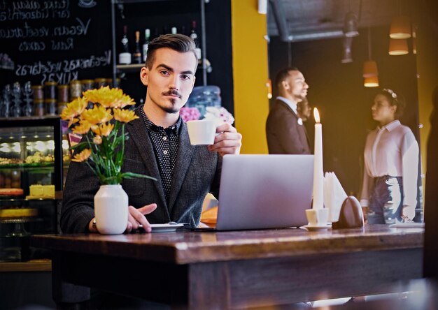 Serious mustache hipster male drinks coffee and using laptop in a cafe.