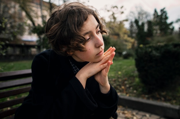 Serious non binary person sitting on a bench thoughtfully