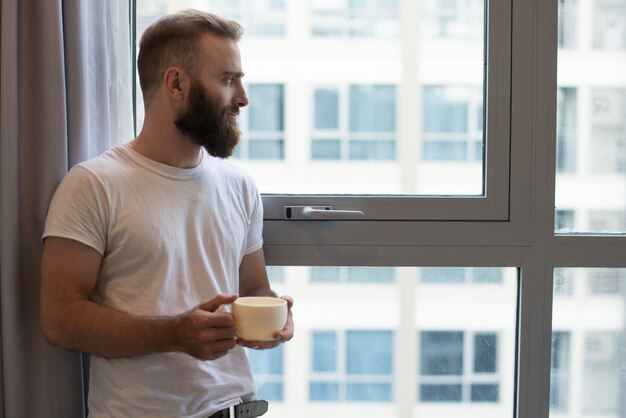 Serious pensive young bearded man drinking coffee