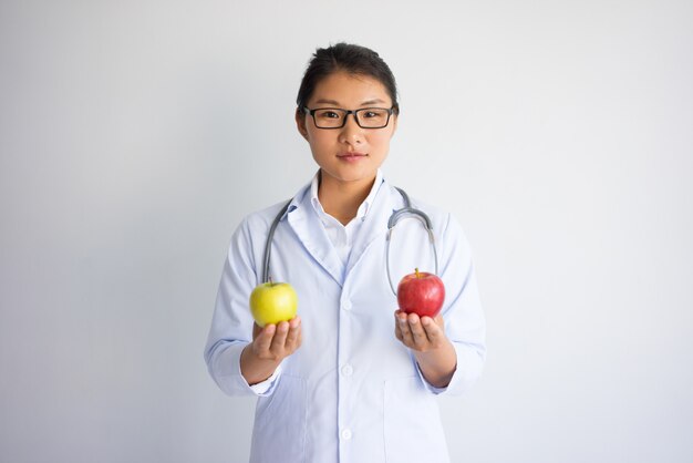 Serious pretty Asian female doctor with red and yellow apple.