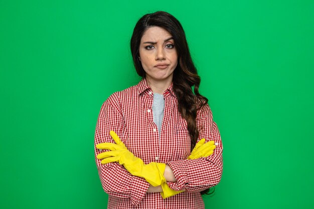 Serious pretty caucasian cleaner woman with rubber gloves standing with crossed arms and looking 
