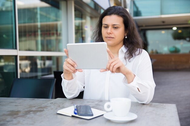 Serious pretty lady reading news on tablet in street cafe