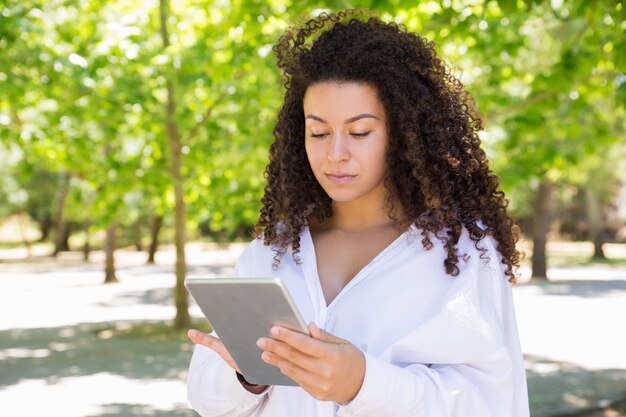 Serious pretty young woman browsing on tablet in park