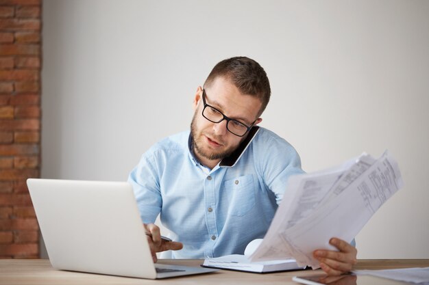 Serious professional businessman talking on phone with customer, holding papers in hand