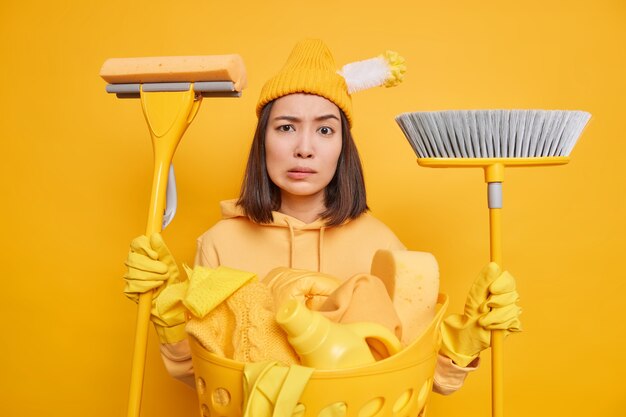 Free photo serious puzzled housewife doesnt know from what to begin cleaning dressed in casual clothes uses mop and broom for washing sweeping floor does laundry keeps house clean. domestic chores concept