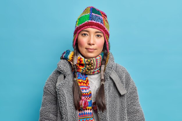 땋은 머리를 가진 심각한 스칸디나비아 여자는 파란색 벽 위에 따뜻한 겨울 옷을 입은 앞에서 침착하게 보입니다.