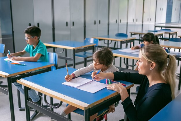 Serious school teacher helping pupils to cope with their task in class