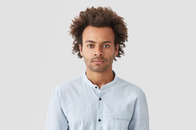 Serious self assured man with curly hair, looks with concentrated expression, dressed in white shirt, listens attentively