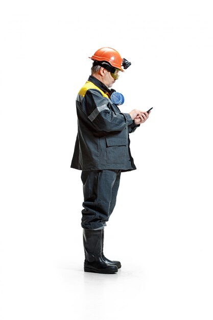 serious senior bearded male miner standing at the camera with smartphone on a white