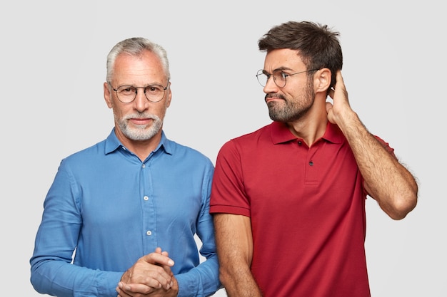 Серьезный старший бородатый мужчина в синей элегантной рубашке разговаривает с сыном, который смотрит на него с недоумением