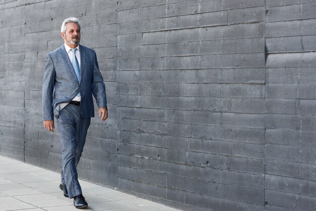 Serious senior businessman walking outside of modern office building.