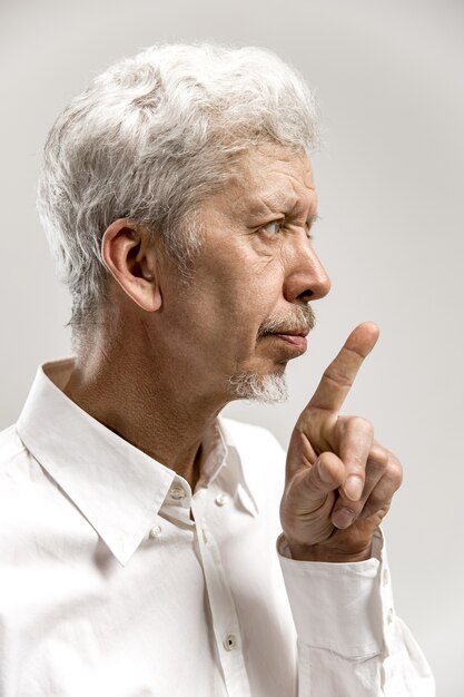 Серьезный старший испуганный мужчина держит указательный палец на губах, пытается сохранить заговор