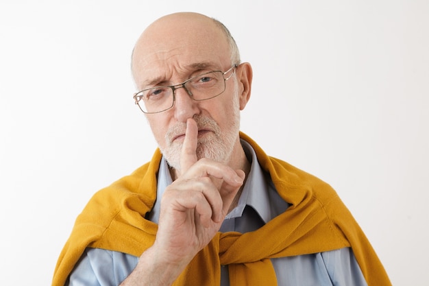 Free photo serious senior mature man placing fore finger on his lips with shhh shushing sign wearing eyeglasses and stylish clothes, keeping some confidential information. gestures, symbols, secret and control