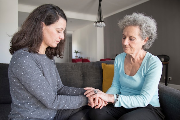 Serious senior woman and her daughter holding hands