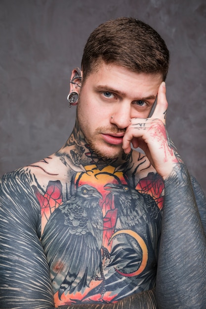 Serious shirtless young man with tattoo on his body looking at camera