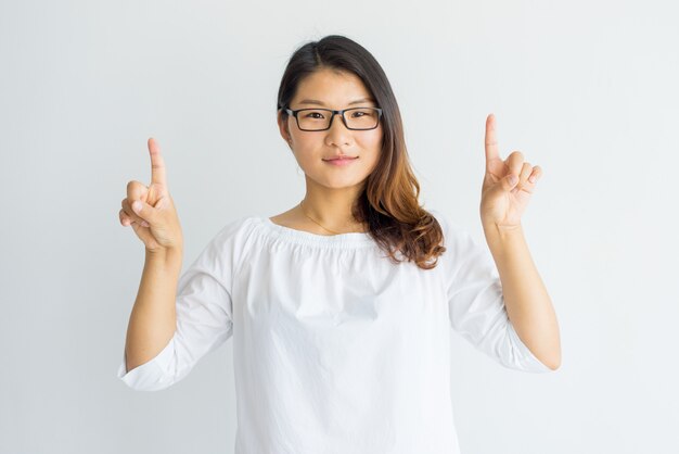 Serious smart Asian girl with highlighted hair pointing up with fingers. 