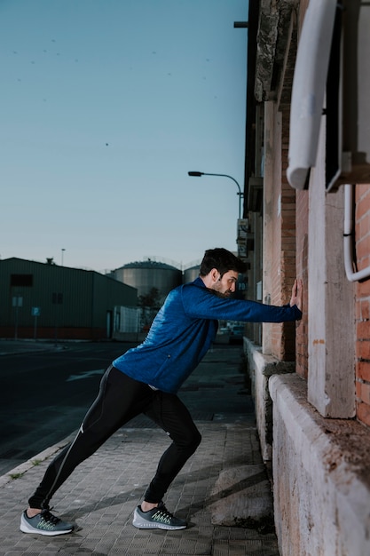 Serious sportsman leaning on wall and warming