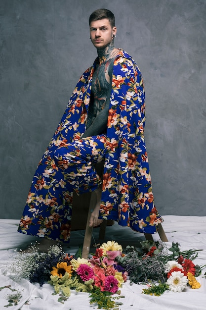 Serious tattooed young man in floral drape looking at camera